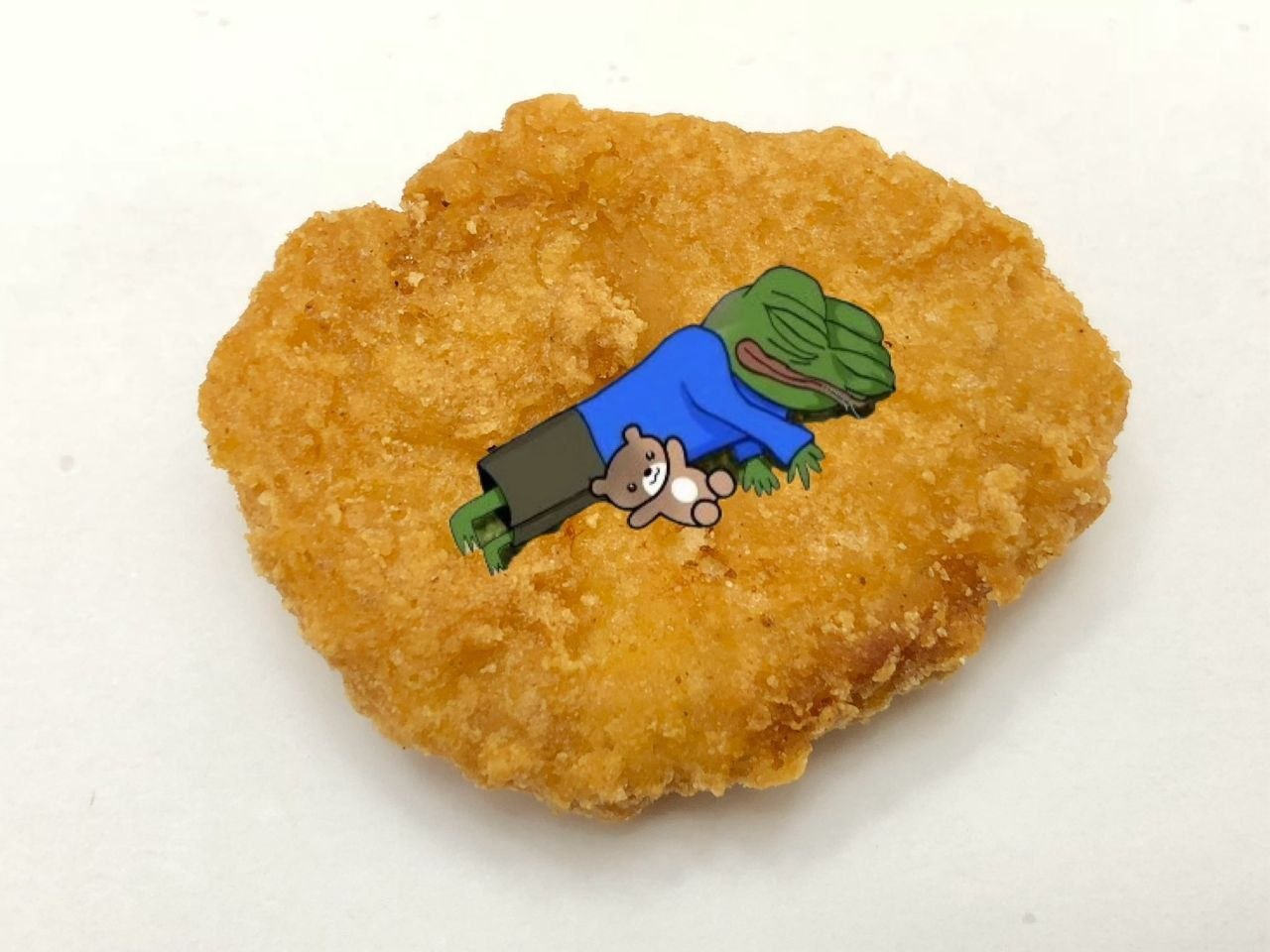Tiny Pepe napping on a chicken patty